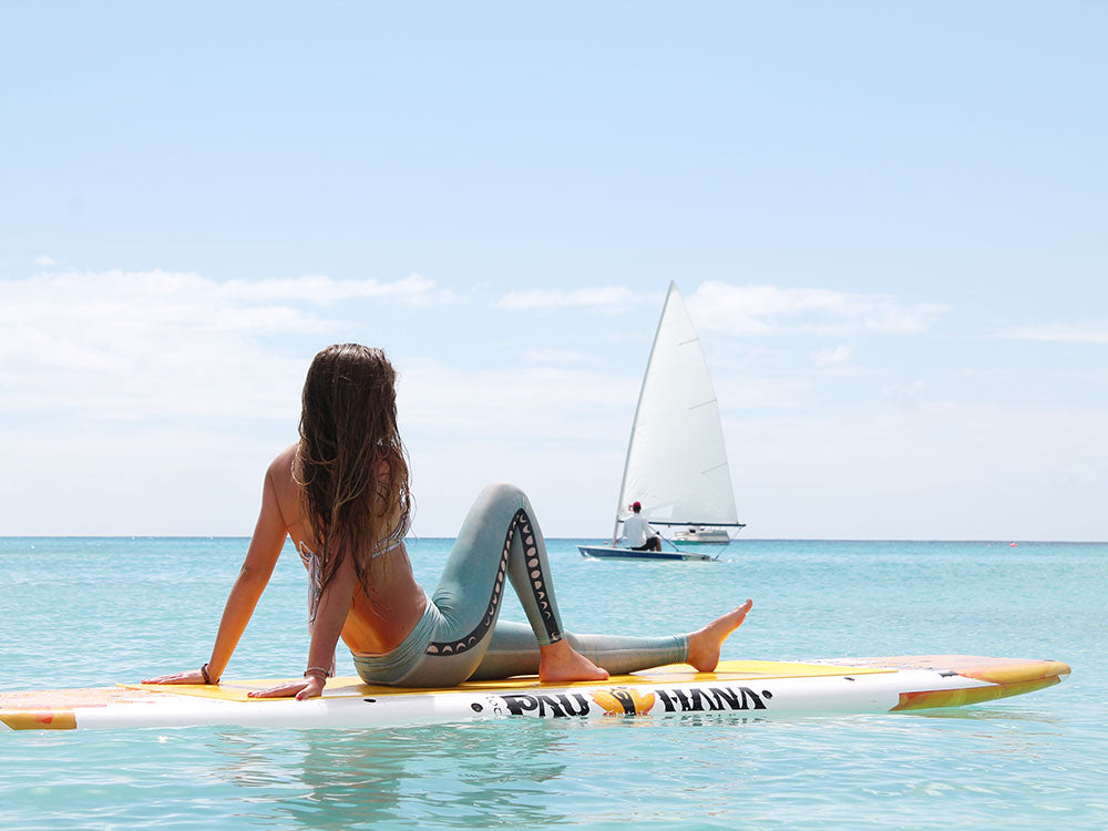 A woman sitting on a paddleboard with a sail boat in the background