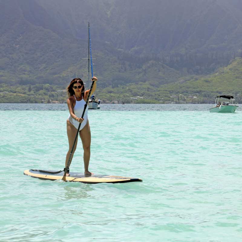 a woman in a white swimsuit paddling a paddleboard past yachts in hawaii