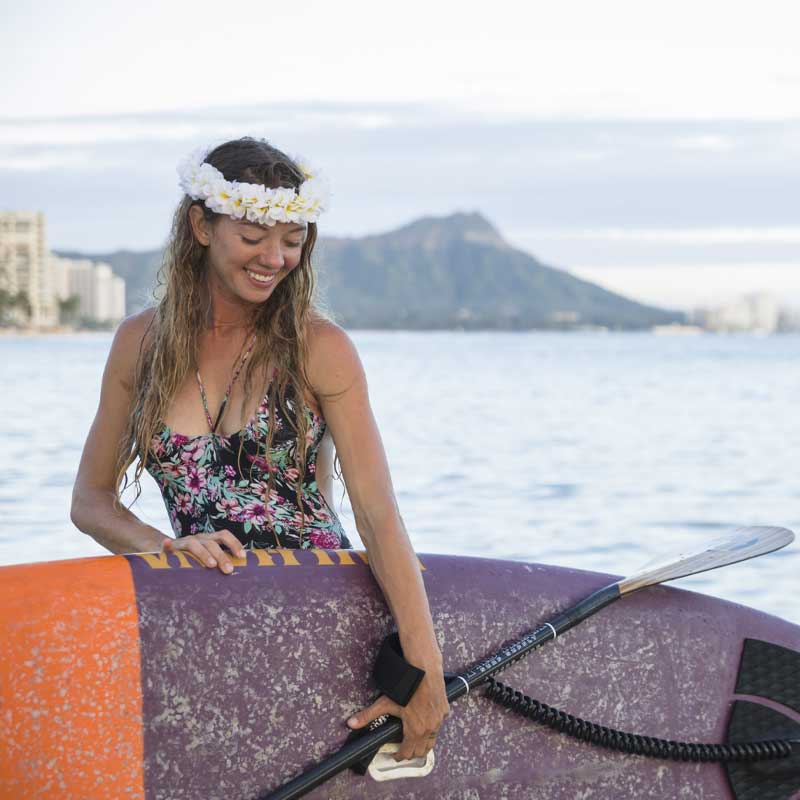 A girl wearing flowers in her hair carrying the carve paddleboard on a beach