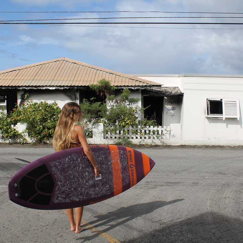 A girl carrying the carve pro paddleboard to the beach past a house in barbados