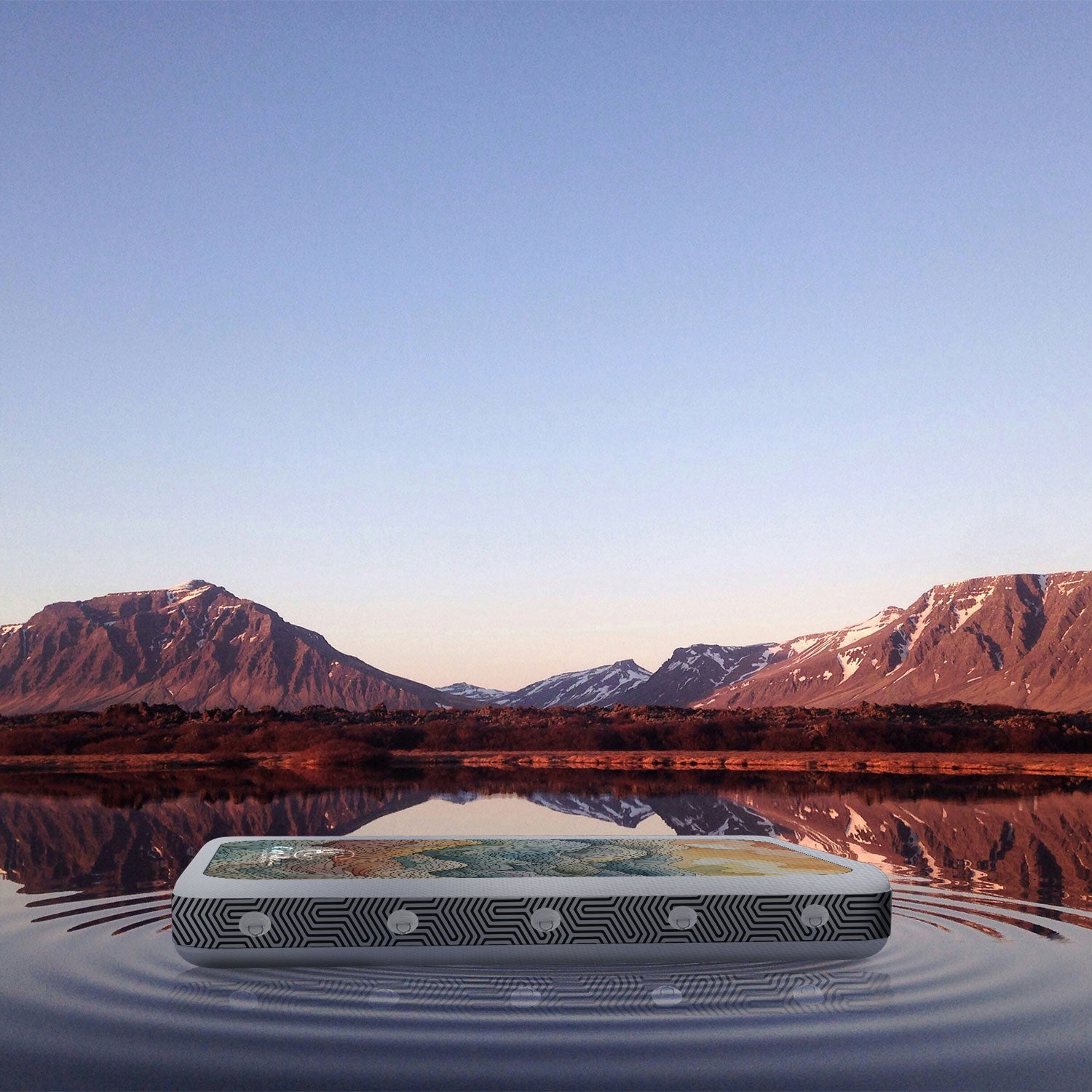 The Cambia adaptable inflatable surface floating on a lake with mountains in the background at sunset