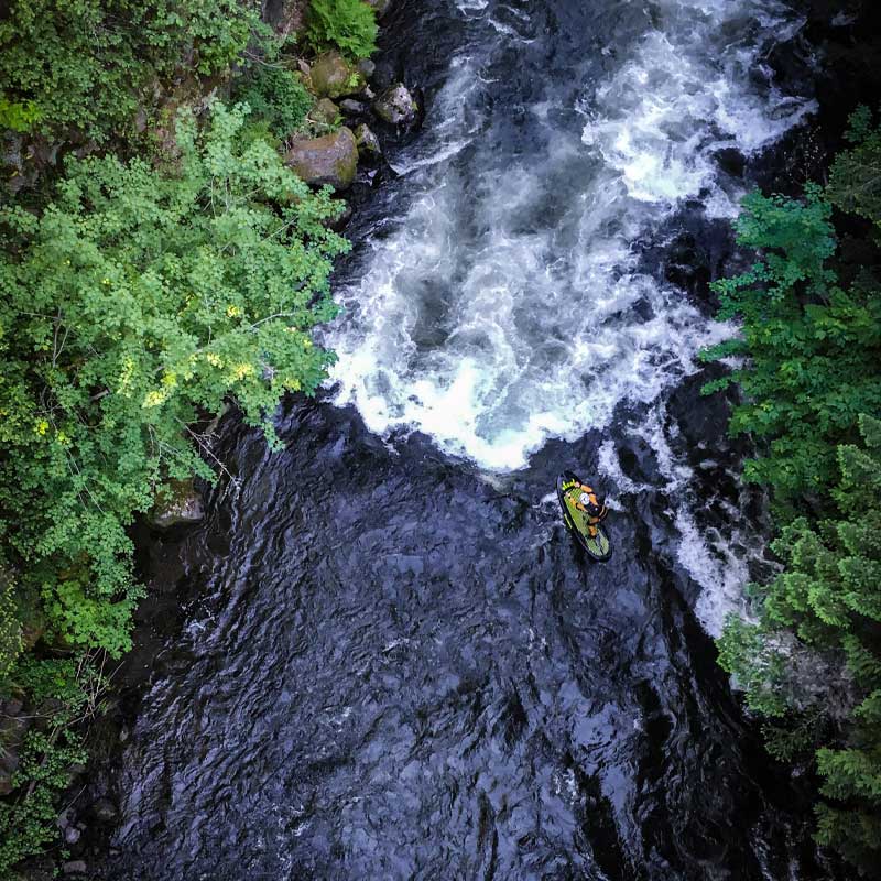 Anaerial image of a guy stand up paddleboarding down some white water rapids 