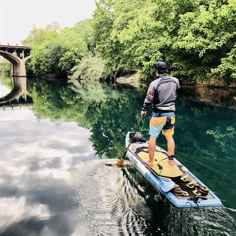 a guy paddleboarding on a river with a bridge in the background