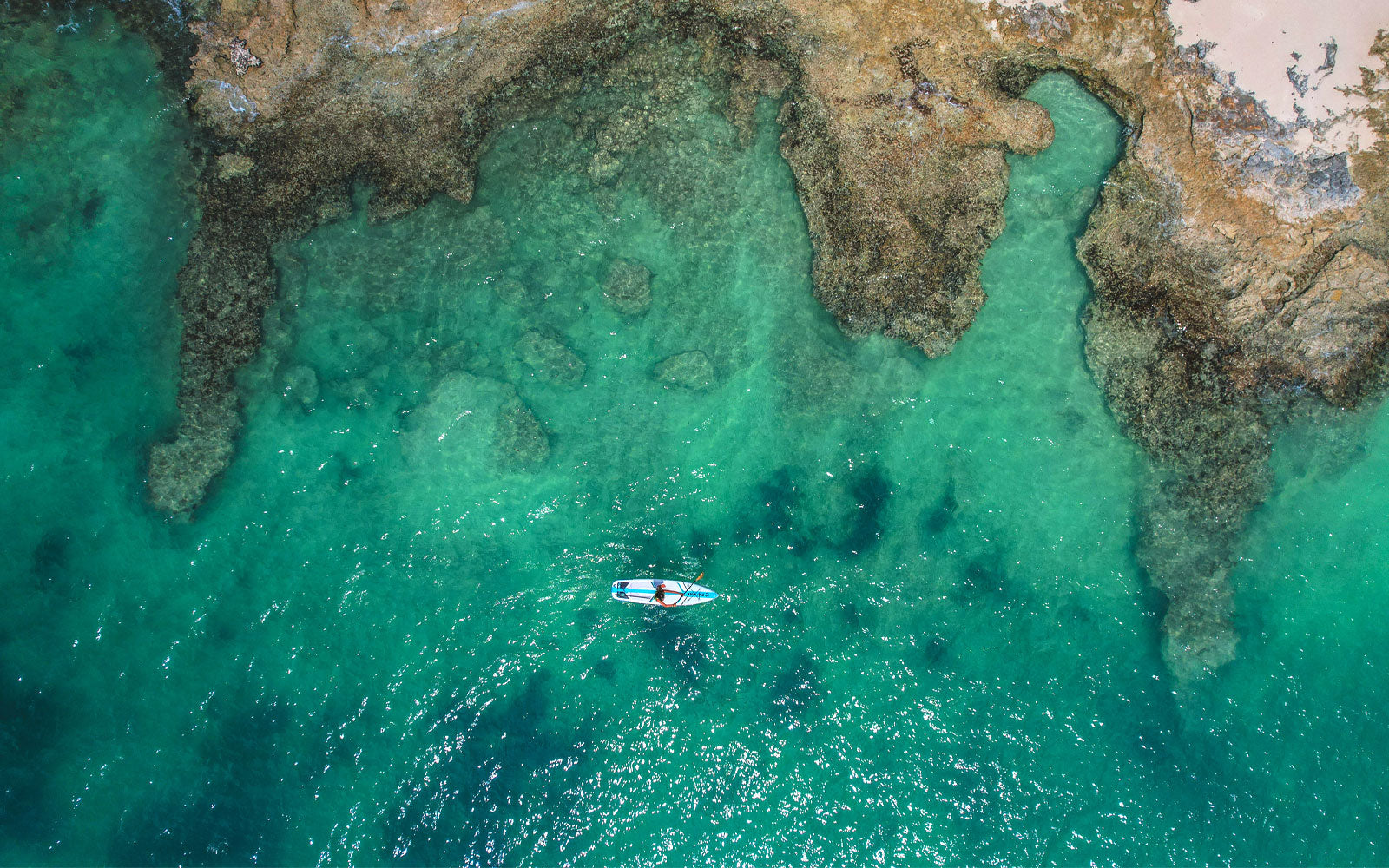 An ariel image of a woman paddling an inflatable paddleboard close to the coastline in Barbuda