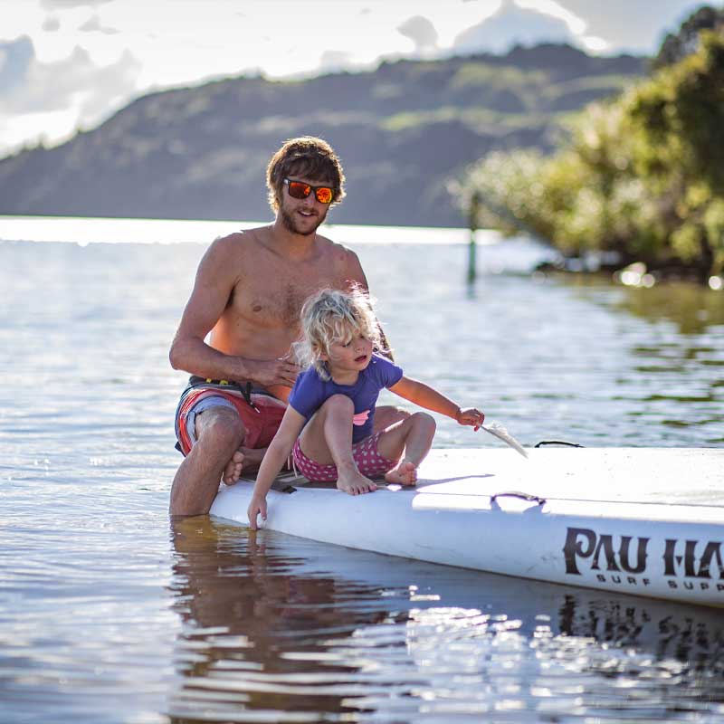 a farther and child sat on the oahu nui inflatable paddleboard on a lake with trees in the background