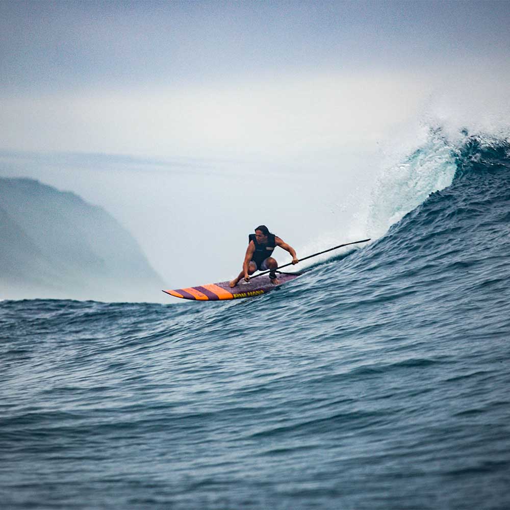 SUP surfing a big wave in hawaii with mountains in the background