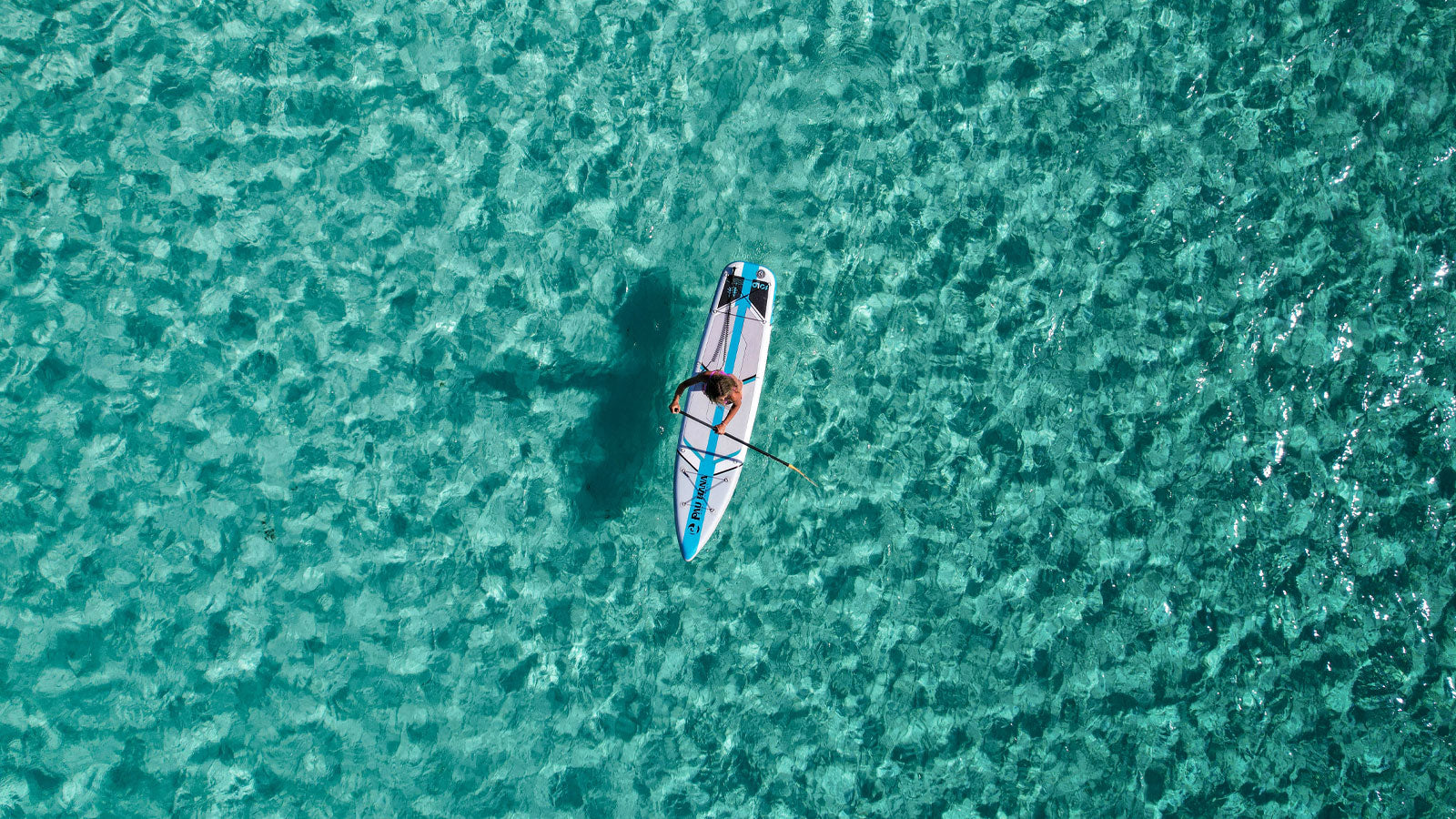 An aerial image of a paddleboarder paddling on clear turquoise waters