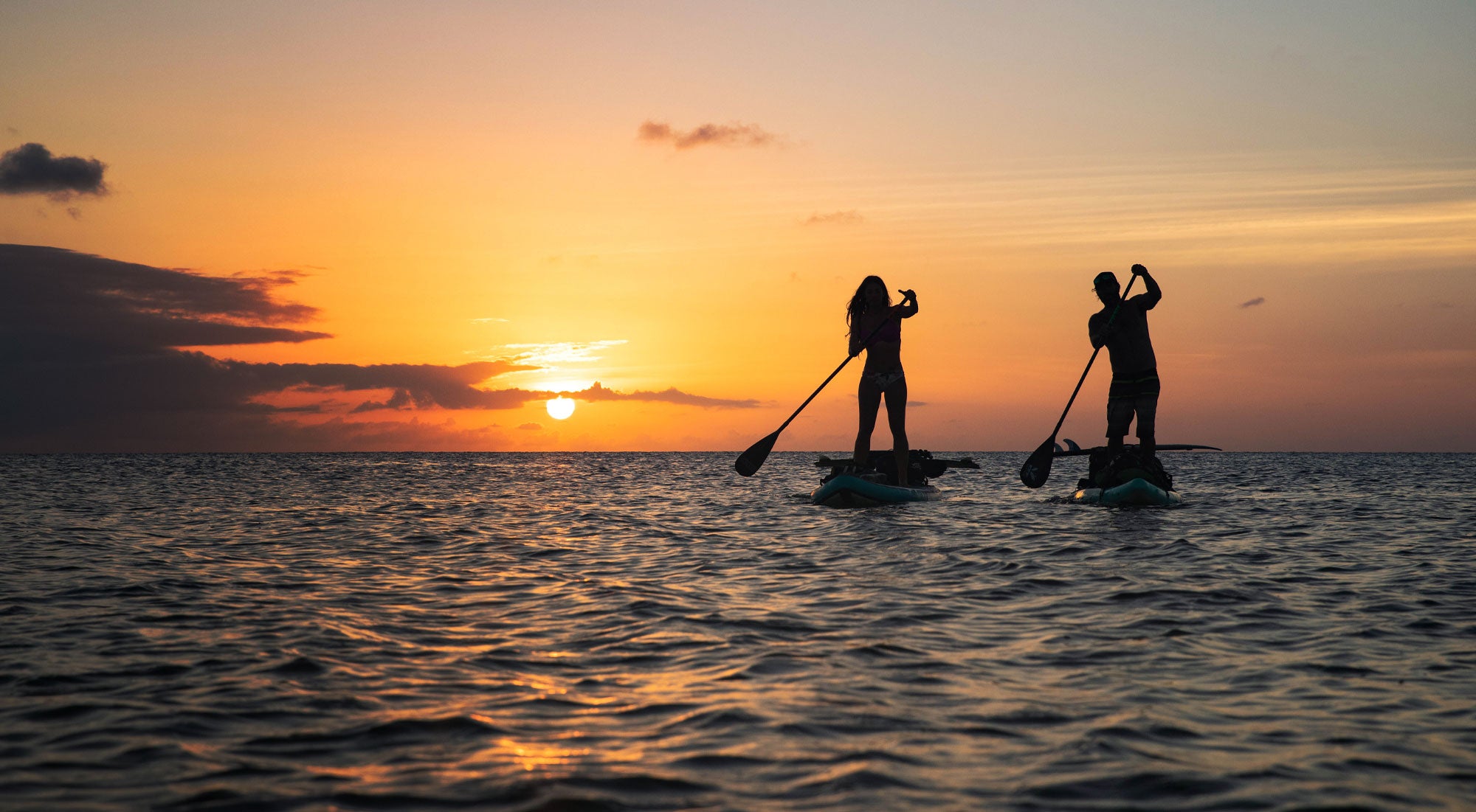 two paddleboarders paddling off into the sunset