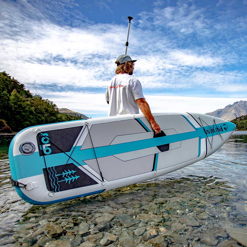 Man holding the Solo SUP Backcountry inflatable paddleboard next to a lake