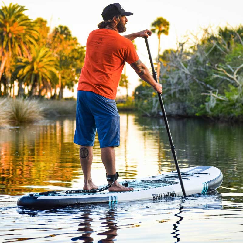 a man stand up paddling at sunset on a river with palm trees in the background