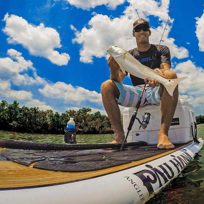 a guy sat on a cool box holding a fish on the big ez angler paddleboard