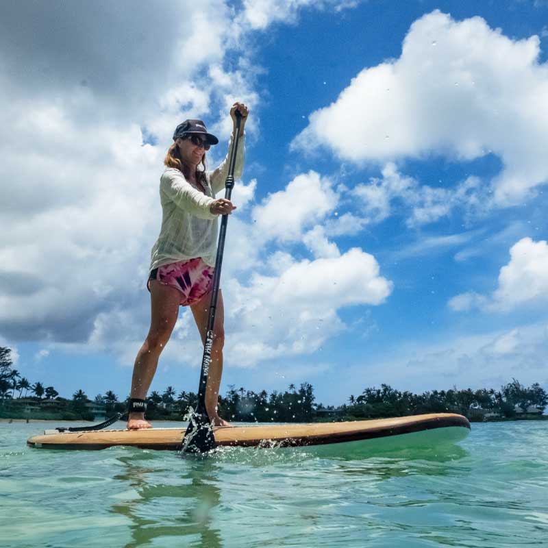 a woman stand up paddling on the sea with trees and the shore in the background