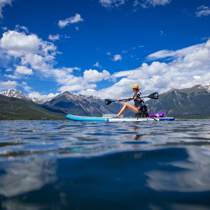 A woman sat on a paddleboard paddling in the rockies