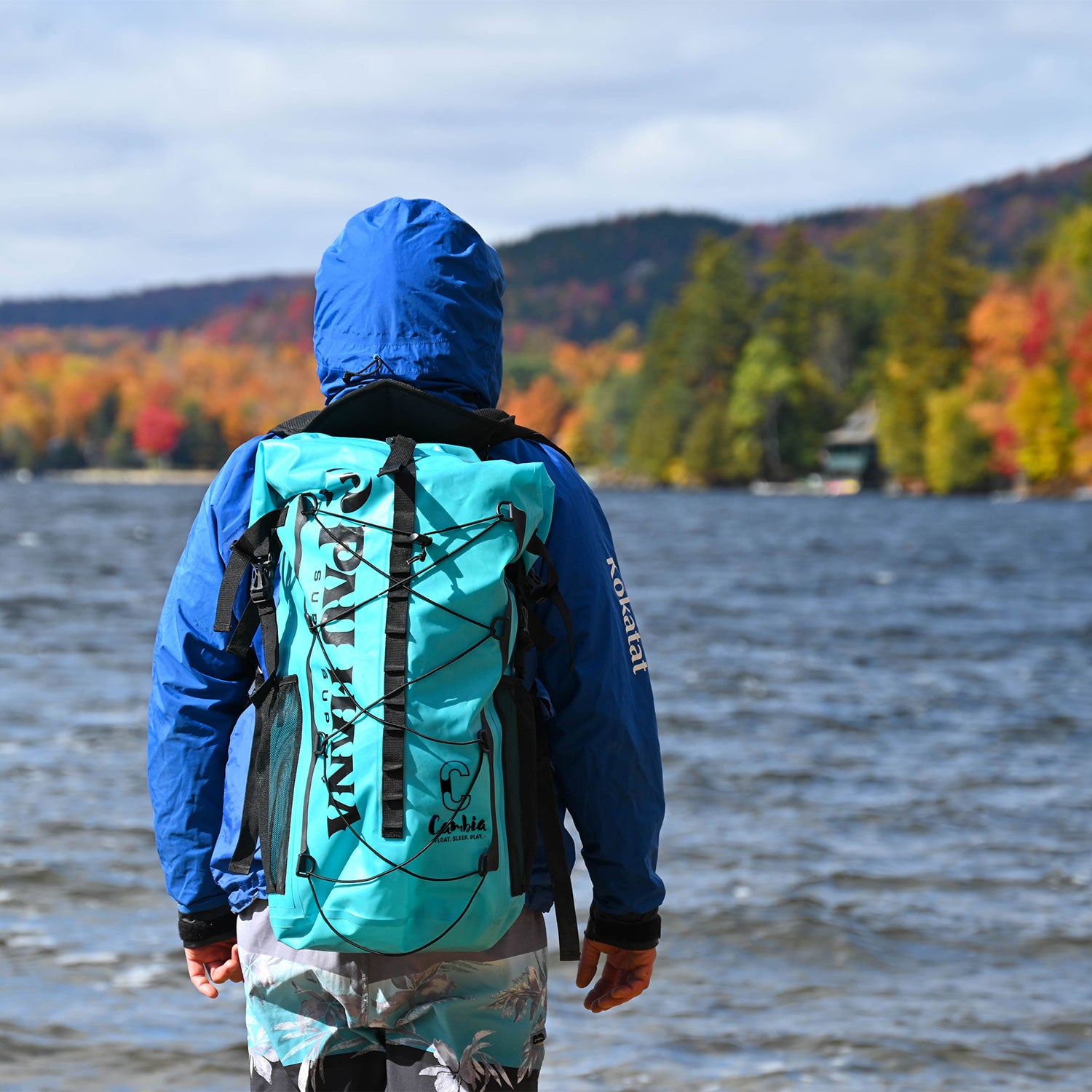 A man standing by a lake with the Cambia backpack on looking out over the water