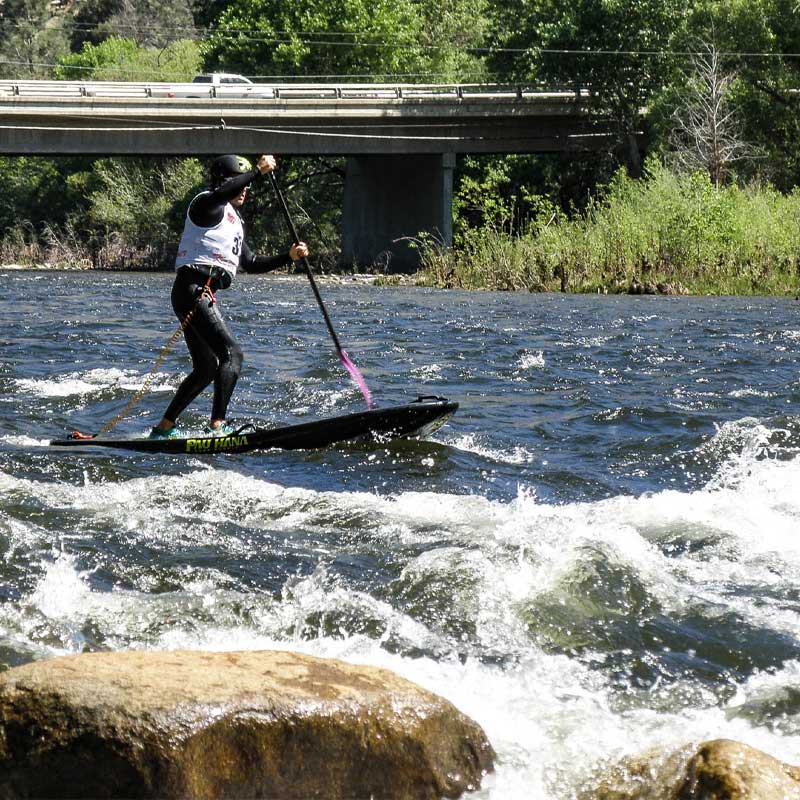 A guy whitewater paddleboarding down a river