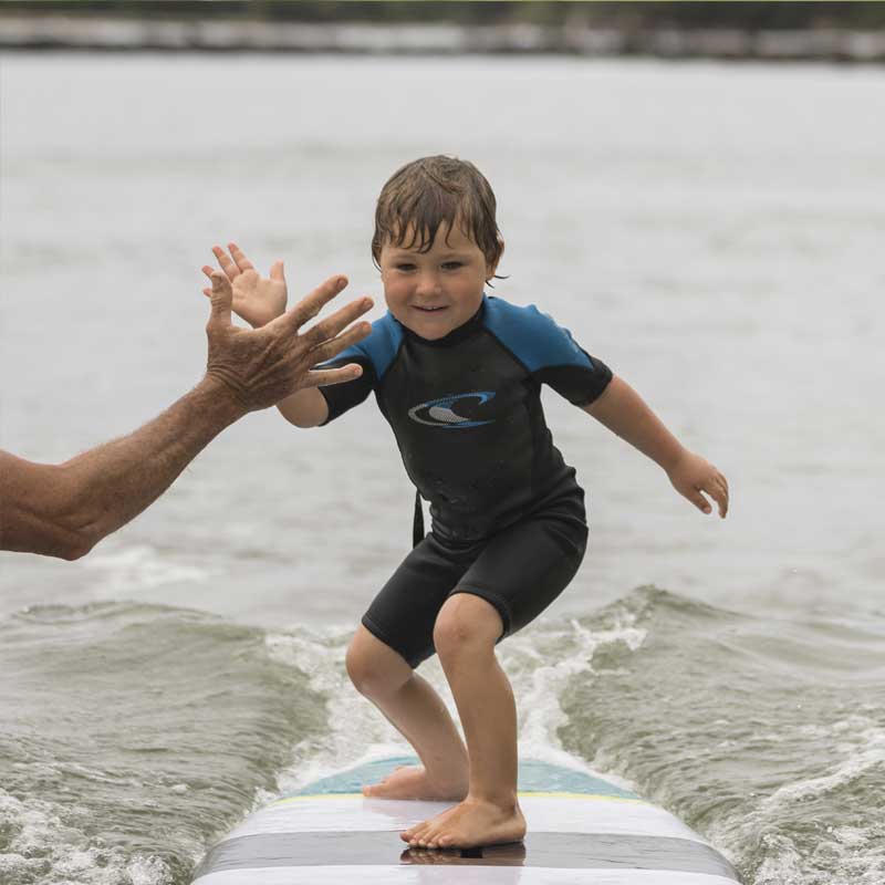 A kid and adult highfiving as the kid surfs past on a paddleboard