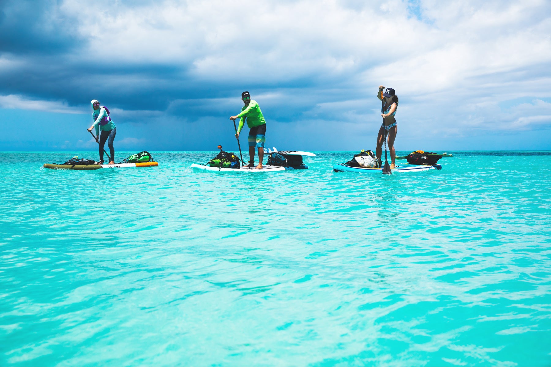 three people stand up paddleboarding on bright blue oceans