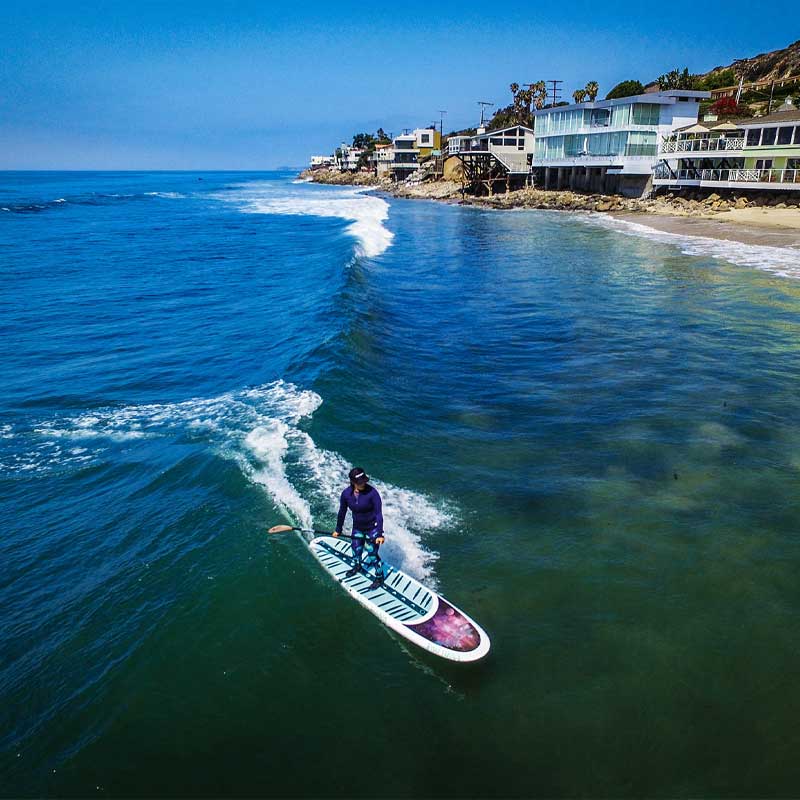 A woman surfing a wave on a paddleboard with beach homes in the background
