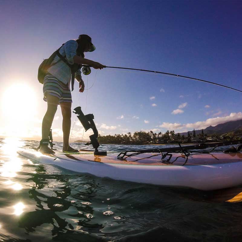 a woman fishing from the navio paddleboard at sunset
