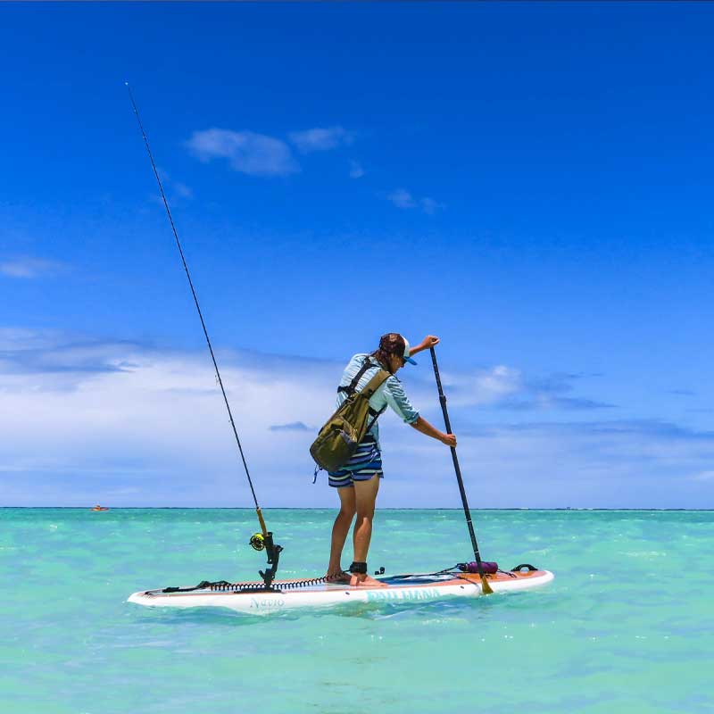 a woman paddling the navio paddleboard with a fishing rod attached to the back