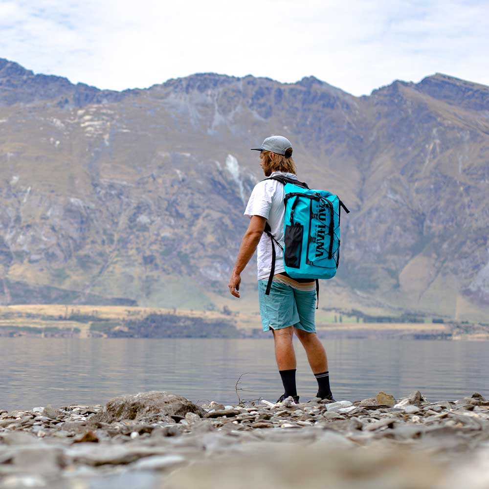 man standing looking over a lake with the solo sup drybag on his back